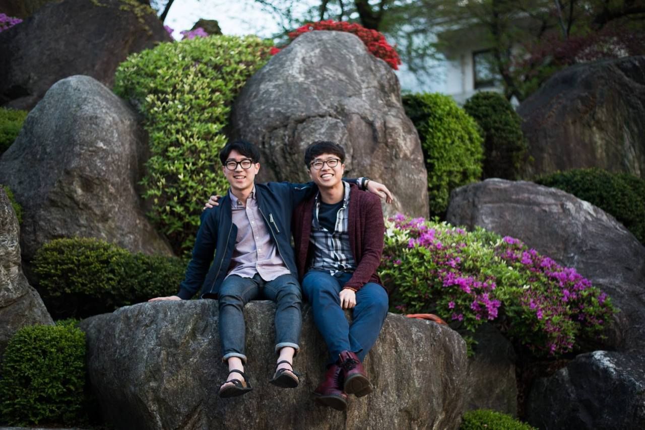 two men sitting on a rock together, smiling